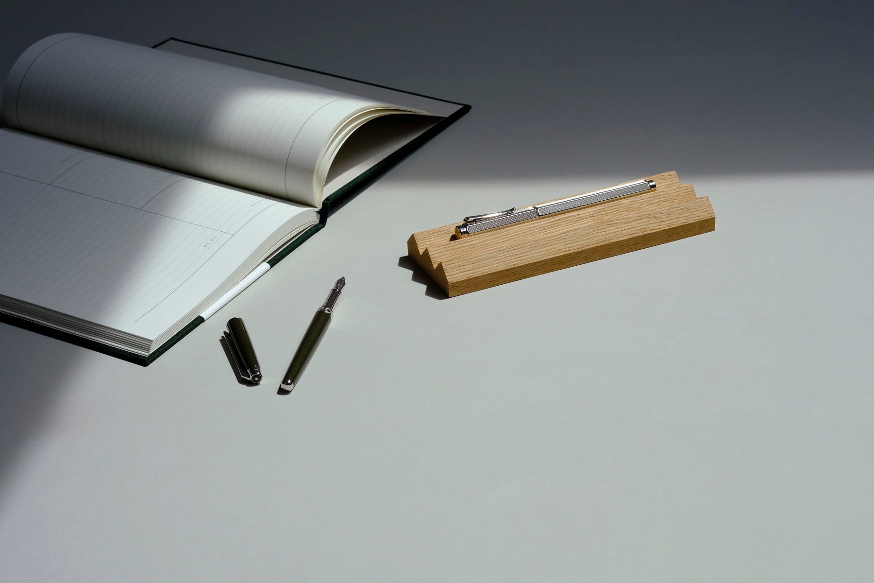 Otwarty planner Work Journal od Notem, a obok drewniana podstawka na przybory do pisania i pióra wieczne marki Caran d'Ache.