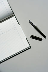 Open Caran d’Ache Léman Slim fountain pen next to a Work Journal notebook on a gray background.
