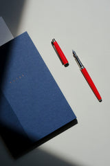 Navy Classic notebook next to an open Caran d’Ache Léman Slim Scarlet Red fountain pen.