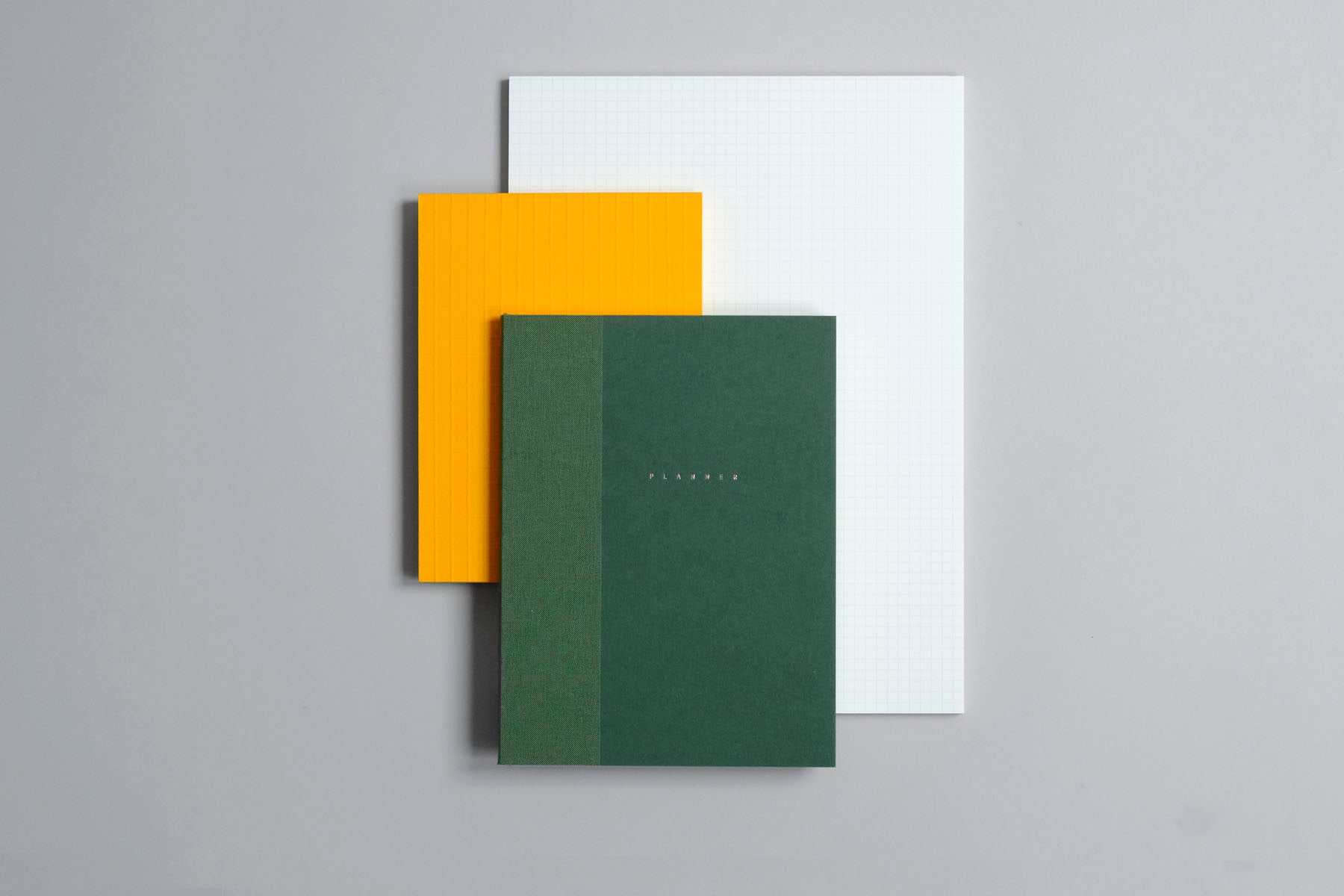 Planner Klasyk w kolorze mech oraz pomarańczowy notes Martina i pad z wyrywanymi kartkami Midori w kratkę.