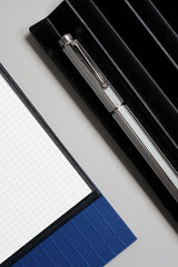 Cap with clip and barrel of the Caran d'Ache Ecridor Milanese Mesh fountain pen on a black metal pen stand.