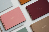 Several photo albums, with a burgundy canvas photo album in the center, bound with a copper-colored spiral.