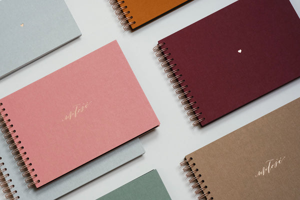 Several photo albums, with a burgundy canvas photo album in the center, bound with a copper-colored spiral.