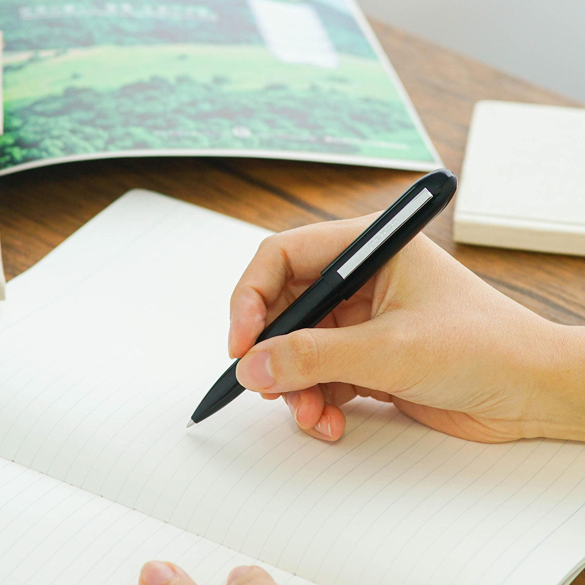 Otwarty, czarny długopis trzymany w dłoni nad notatnikiem.