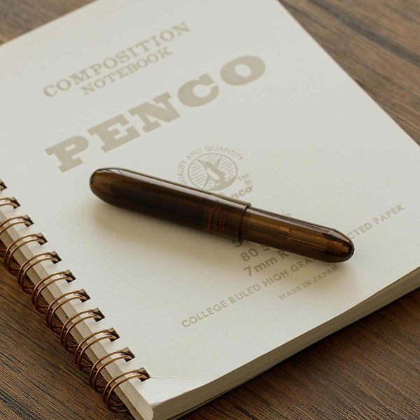 A Bullet ballpoint pen by the Penco brand made of semi-transparent plastic, lying on a spiral notebook.