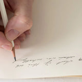 A beige pencil held in a hand above a sheet of paper.