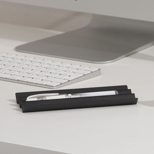 A black steel NAKA pen holder with a white pen placed on it.