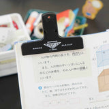 A black plastic clip with a white Penco logo, holding together the pages of a notebook.