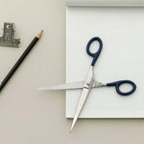 Steel scissors with navy handles against a grid notebook background.