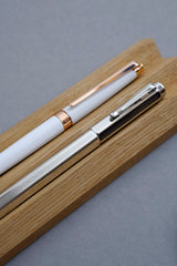 White Caran d’Ache Léman Slim fountain pen and Ecridor Chevron fountain pen on an oak stand.