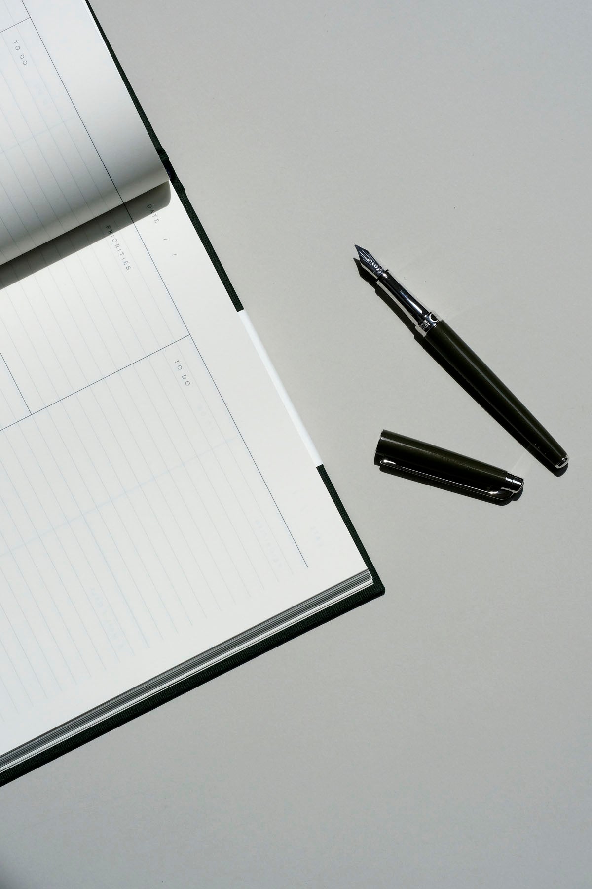 Otwarte pióro wieczne Leman Slim obok notatnika Work Journal na szarym tle.