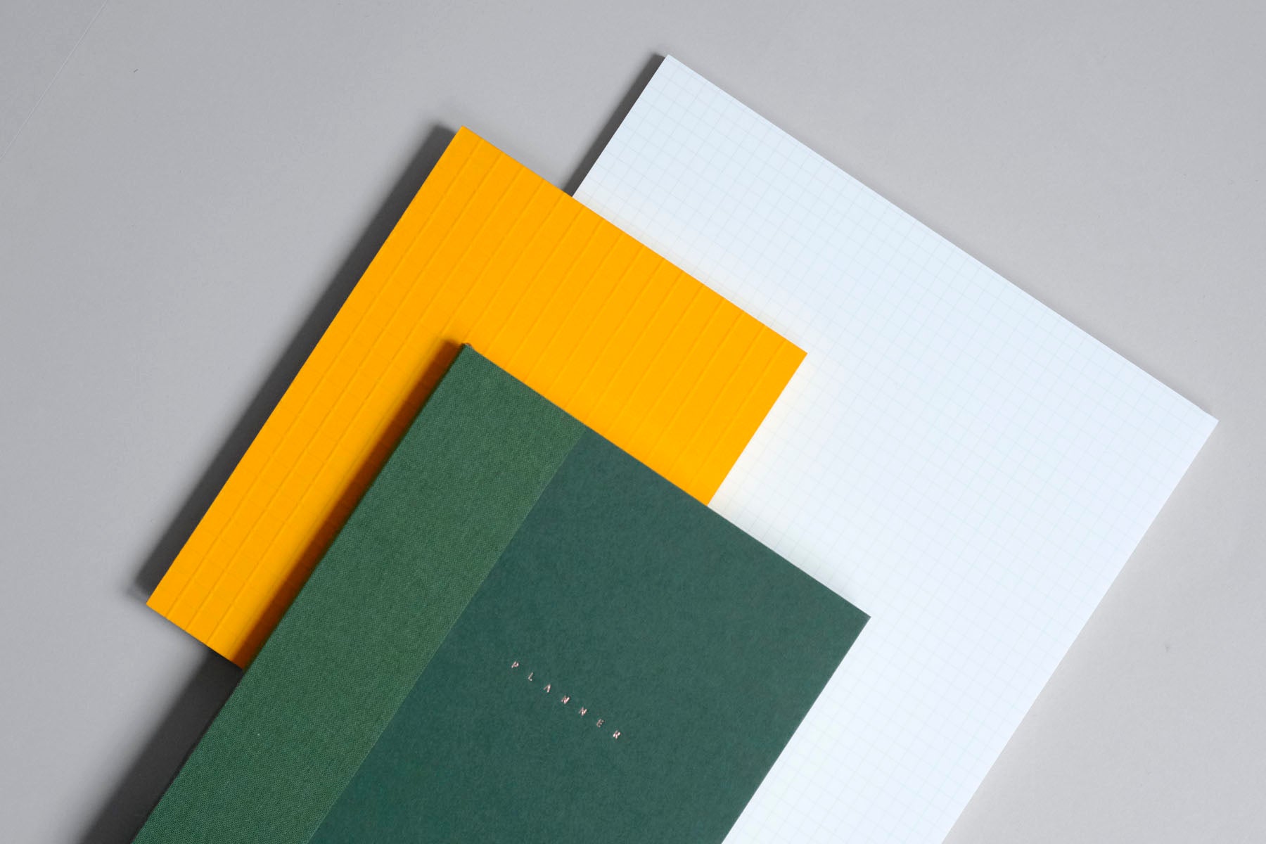 Planner Klasyk w kolorze zielonym, pod nim pomarańczowy notes Martina oraz pad z wyrywanymi kartkami Midori.