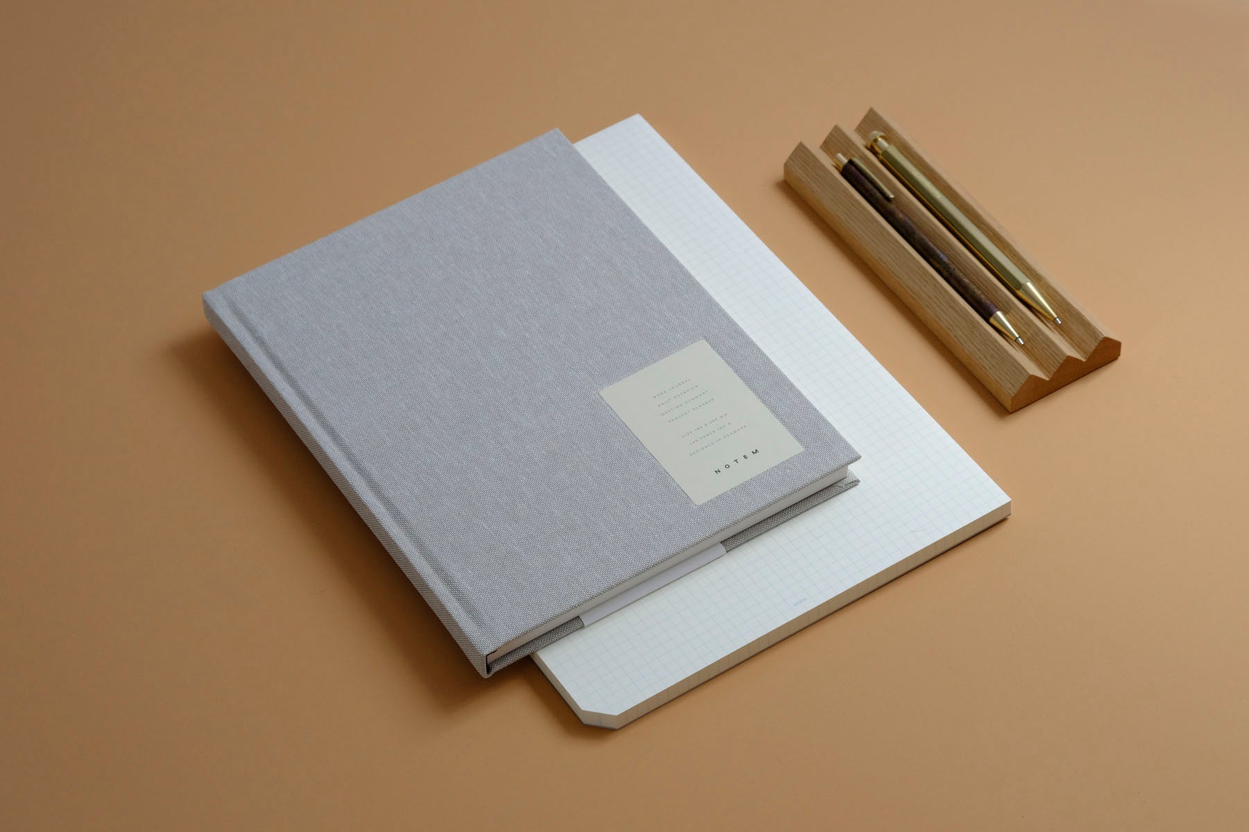 Planner Work Journal wraz z dębową podstawką na przybory do pisania, mosiężnymi długopisami i padem Midori w kratkę.