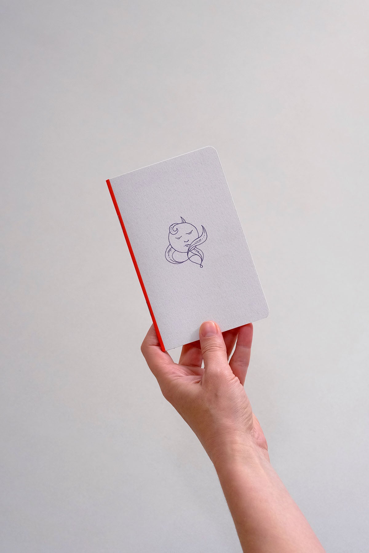 Mały notatnik w kolorze jasnoszarym z granatową ilustracją, trzymany w dłoni.
