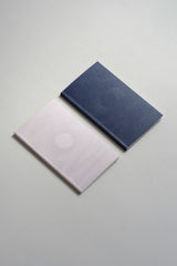 Two notebooks on a grey background: a beige one with a full moon motif and a navy one with a new moon motif.