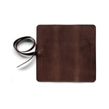 The unfolded chocolate brown pen roll is secured with a leather strap.