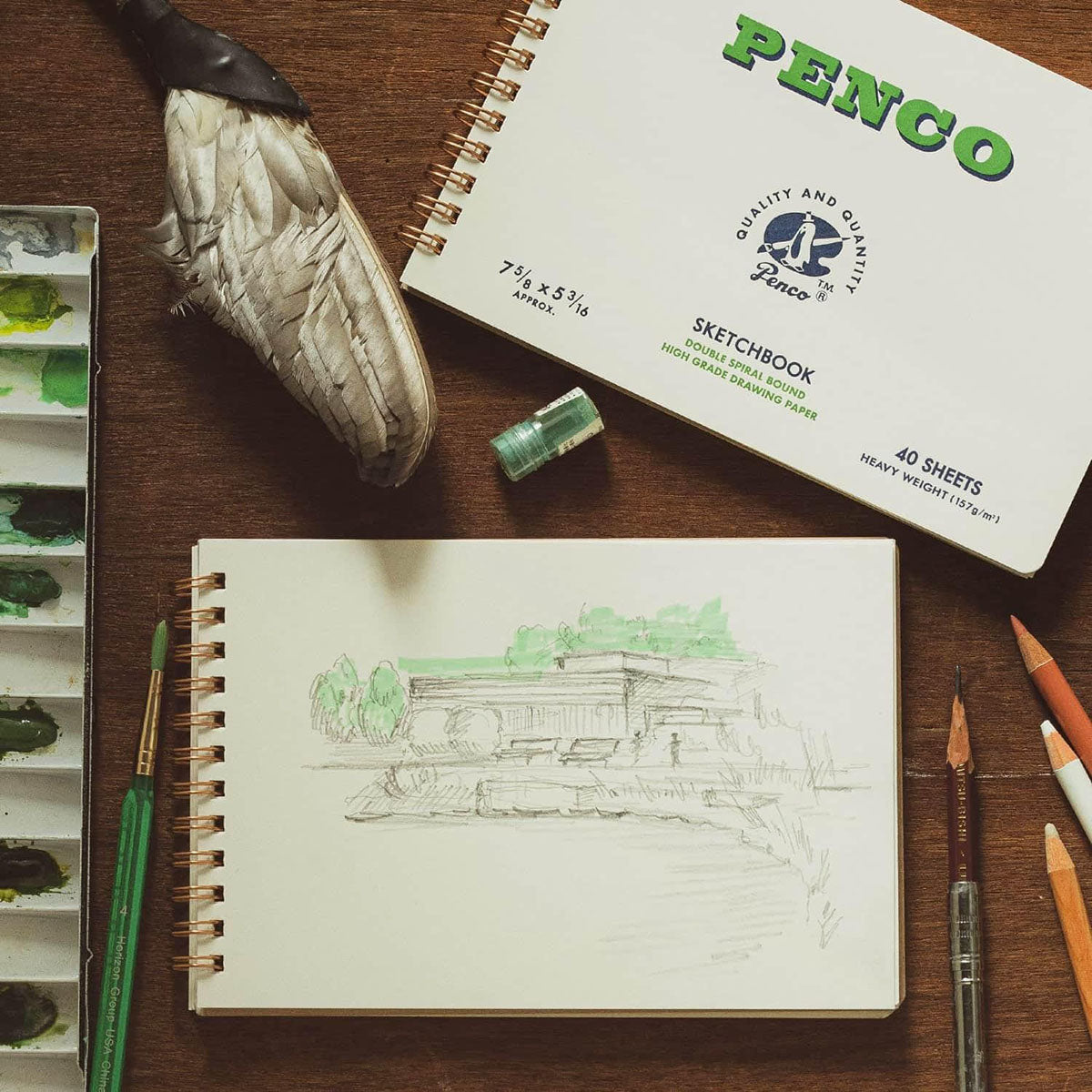 Ilustracja narysowana na jasnej karcie szkicownika oraz inne akcesoria rysunkowe.